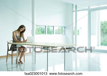 Woman sitting at table, using laptop computer, smiling View Large Photo Image Stock Image - Woman sitting at table, using laptop computer, smiling. Fotosearch