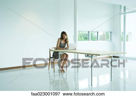 Woman sitting at table, using laptop computer, looking down View Large Photo Image Stock Photo - Woman sitting at table, using laptop computer, looking down. Fotosearch