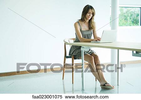 Woman sitting at table using laptop computer, smiling, full length View Large Photo Image Stock Photography - Woman sitting at table using laptop computer, smiling, full length. Fotosearch