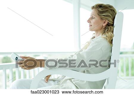 Woman sitting in chair on porch, eyes closed, holding cell phone View Large Photo Image Stock Image - Woman sitting in chair on porch, eyes closed, holding cell phone. Fotosearch