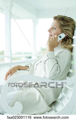 Woman sitting in chair on porch, using cell phone, smiling View Large Photo Image Stock Photograph - Woman sitting in chair on porch, using cell phone, smiling. Fotosearch