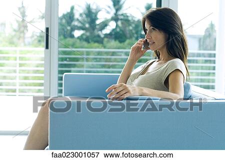 Woman sitting on couch, using cell phone, looking up View Large Photo Image Stock Photo - Woman sitting on couch, using cell phone, looking up. Fotosearch
