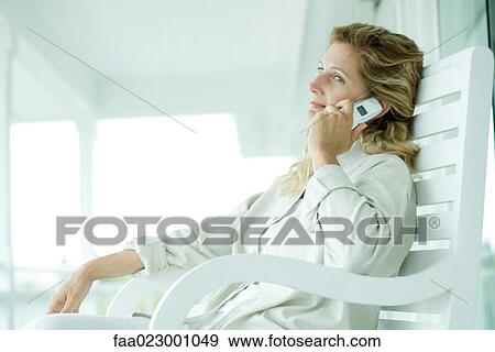 Stock Photo - Woman sitting on porch using cell phone, smiling, looking away. Fotosearch