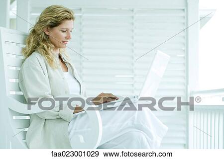 Stock Photo - Woman sitting on porch using laptop computer, smiling. Fotosearch