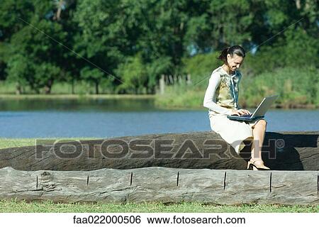 Woman sitting on tree trunk, using laptop View Large Photo Image Stock Photograph - Woman sitting on tree trunk, using laptop. Fotosearch