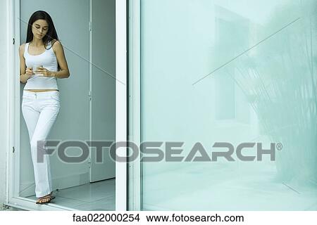 Woman standing in doorway, holding cup, full length portrait View Large Photo Image Picture - Woman standing in doorway, holding cup, full length portrait. Fotosearch