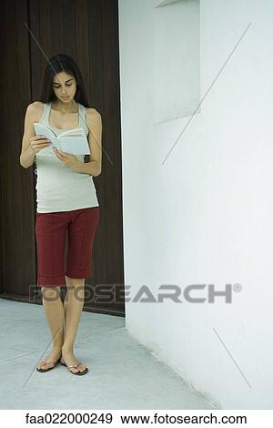 Stock Photo - Woman standing reading book, full length portrait. Fotosearch