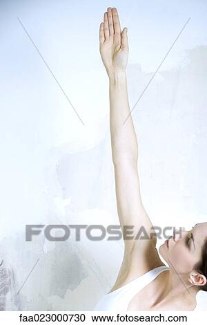 Stock Image - Woman standing with one arm raised, looking up, cropped view. Fotosearch