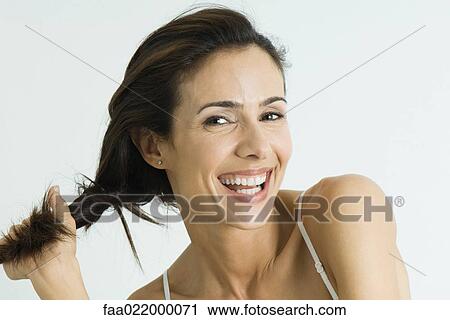 Stock Image - Woman twisting hair to the side, smiling at camera, portrait. Fotosearch