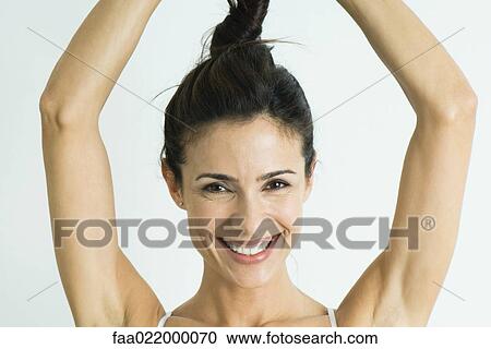 Stock Image - Woman twisting hair up above head, smiling at camera, portrait. Fotosearch