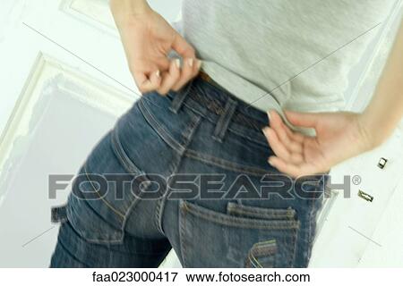 Woman untucking shirt from waist of jeans, close-up, rear view View Large Photo Image Stock Photo - Woman untucking shirt from waist of jeans, close-up, rear view. Fotosearch
