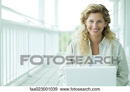 Woman using laptop computer on porch, smiling at camera, portrait View Large Photo Image Stock Photo - Woman using laptop computer on porch, smiling at camera, portrait. Fotosearch