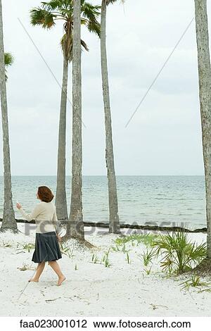 Woman walking on beach, looking at cell phone, full length View Large Photo Image Stock Image - Woman walking on beach, looking at cell phone, full length. Fotosearch