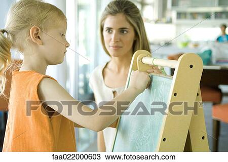 Woman watching little girl draw on chalkboard View Large Photo Image Stock Image - Woman watching little girl draw on chalkboard. Fotosearch