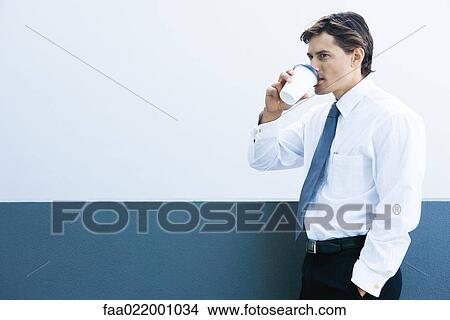Picture - Young businessman drinking hot beverage, hand in pocket, side view. Fotosearch