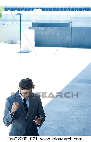Stock Image - Young businessman looking at cell phone, smiling, high angle view. Fotosearch