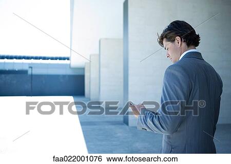 Stock Photograph - Young businessman looking at cell phone, rear view. Fotosearch
