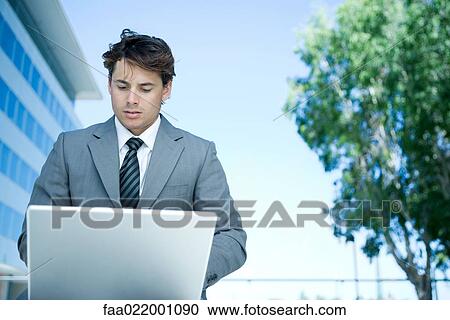 Young businessman outdoors, using laptop computer, looking down View Large Photo Image Stock Image - Young businessman outdoors, using laptop computer, looking down. Fotosearch
