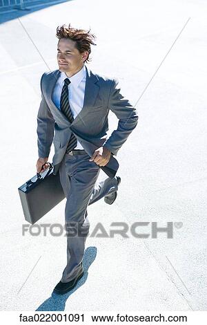 Young businessman running outdoors, carrying briefcase, smiling View Large Photo Image Stock Image - Young businessman running outdoors, carrying briefcase, smiling. Fotosearch
