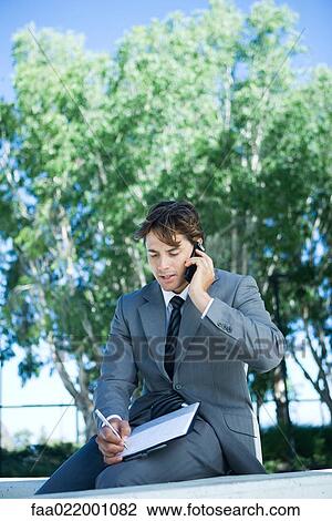 Young businessman sitting outdoors using laptop computer, writing View Large Photo Image Stock Image - Young businessman sitting outdoors using laptop computer, writing. Fotosearch