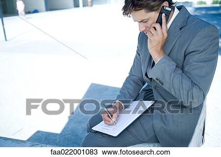 Stock Image - Young businessman sitting outdoors using laptop computer, writing, close-up. Fotosearch