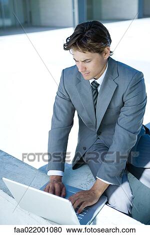 Stock Image - Young businessman sitting, using laptop computer, looking down. Fotosearch