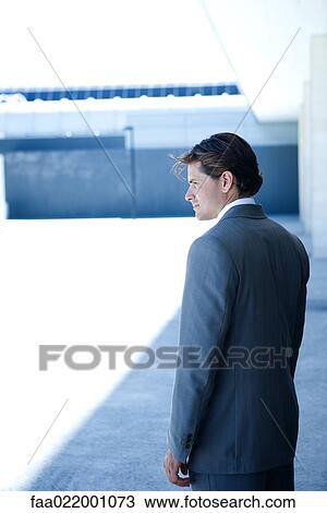 Stock Image - Young businessman standing, looking away, three quarter length. Fotosearch