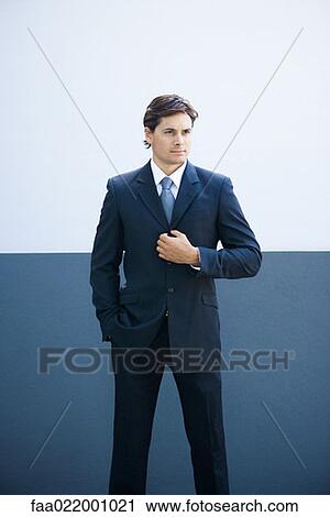 Stock Image - Young businessman standing, wearing full suit, portrait. Fotosearch