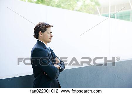 Young businessman standing with arms folded, looking away View Large Photo Image Stock Image - Young businessman standing with arms folded, looking away. Fotosearch