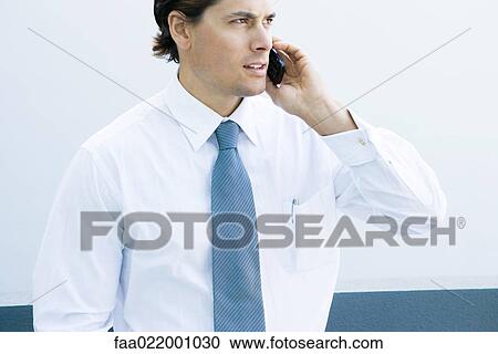Stock Image - Young businessman using cell phone, waist up, cropped view. Fotosearch