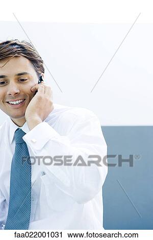 Stock Image - Young businessman using cell phone, smiling, cropped view. Fotosearch
