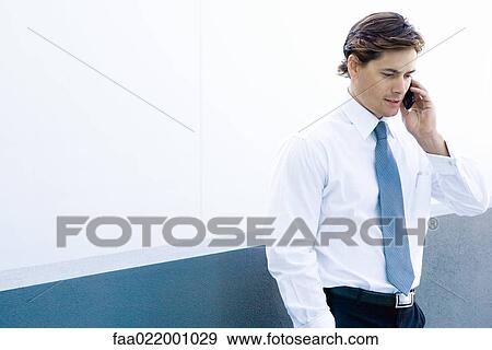Stock Photo - Young businessman using cell phone, waist up. Fotosearch