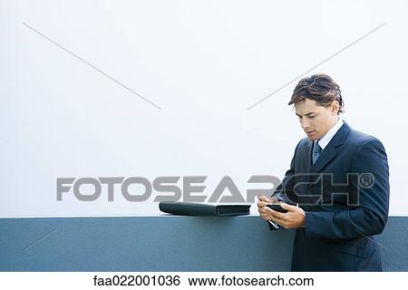 Young businessman using palmtop, looking down View Large Photo Image Stock Photograph - Young businessman using palmtop, looking down. Fotosearch