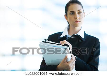 Picture - Young businesswoman holding binder, writing, looking away. Fotosearch