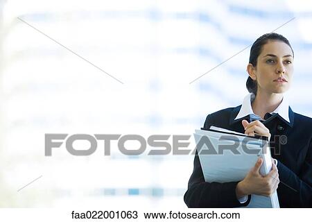 Young businesswoman holding binder, looking away, waist up View Large Photo Image Stock Image - Young businesswoman holding binder, looking away, waist up. Fotosearch