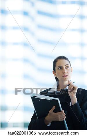 Stock Photography - Young businesswoman holding file, looking up, waist up. Fotosearch