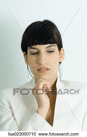 Stock Image - Young businesswoman, holding hand under chin, looking away, portrait. Fotosearch