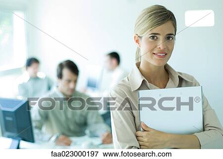 Young businesswoman holding laptop in front of chest in office, smiling at camera, portrait View Large Photo Image Stock Photo - Young businesswoman holding laptop in front of chest in office, smiling at camera, portrait. Fotosearch