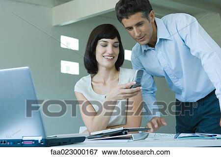Young businesswoman holding up cell phone to mature male colleague, smiling View Large Photo Image Stock Photo - Young businesswoman holding up cell phone to mature male colleague, smiling. Fotosearch
