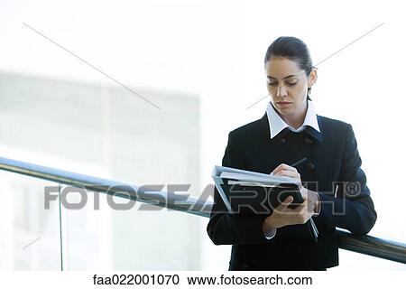 Young businesswoman looking at binder, writing, waist up View Large Photo Image Stock Image - Young businesswoman looking at binder, writing, waist up. Fotosearch