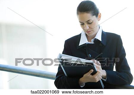 Stock Photo - Young businesswoman looking at binder, writing, waist up. Fotosearch