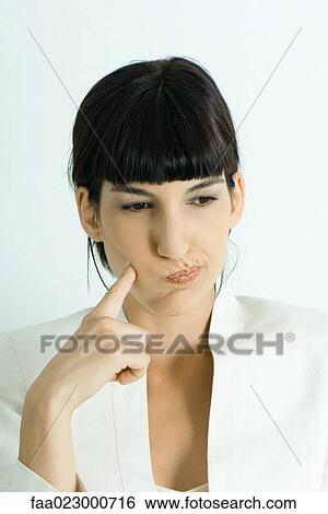 Young businesswoman puffing cheeks out, holding finger to cheek, looking away, portrait View Large Photo Image Stock Photograph - Young businesswoman puffing cheeks out, holding finger to cheek, looking away, portrait. Fotosearch