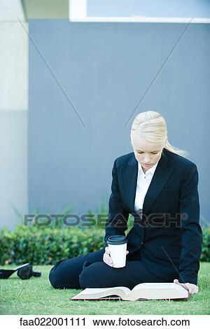 Young businesswoman sitting on the ground outdoors, reading book, holding hot beverage View Large Photo Image Stock Image - Young businesswoman sitting on the ground outdoors, reading book, holding hot beverage. Fotosearch