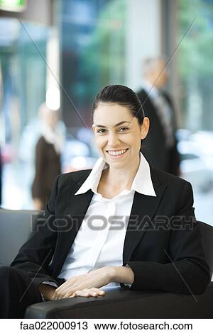 Stock Image - Young businesswoman sitting, smiling at camera, portrait. Fotosearch