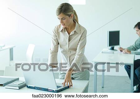 Young businesswoman standing at desk, using laptop View Large Photo Image Stock Photograph - Young businesswoman standing at desk, using laptop. Fotosearch