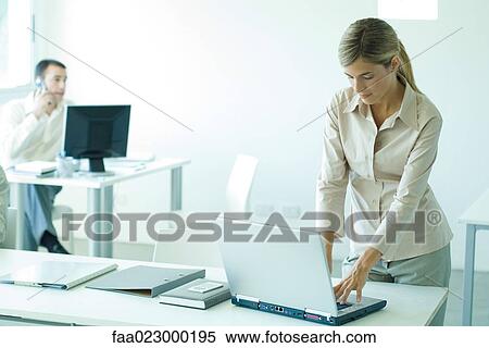 Young businesswoman standing at desk, using laptop View Large Photo Image Stock Photography - Young businesswoman standing at desk, using laptop. Fotosearch