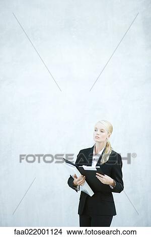 Young businesswoman standing, holding file, looking away View Large Photo Image Picture - Young businesswoman standing, holding file, looking away. Fotosearch