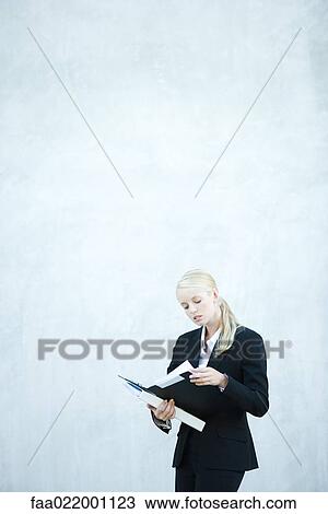 Stock Image - Young businesswoman standing, looking at file, three quarter length. Fotosearch