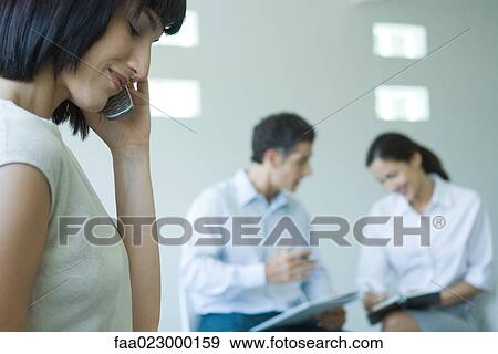 Young businesswoman using cell phone, colleagues working in background View Large Photo Image Stock Photo - Young businesswoman using cell phone, colleagues working in background. Fotosearch