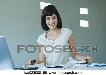 Young businesswoman working at desk, looking down, smiling View Large Photo Image Stock Photograph - Young businesswoman working at desk, looking down, smiling. Fotosearch